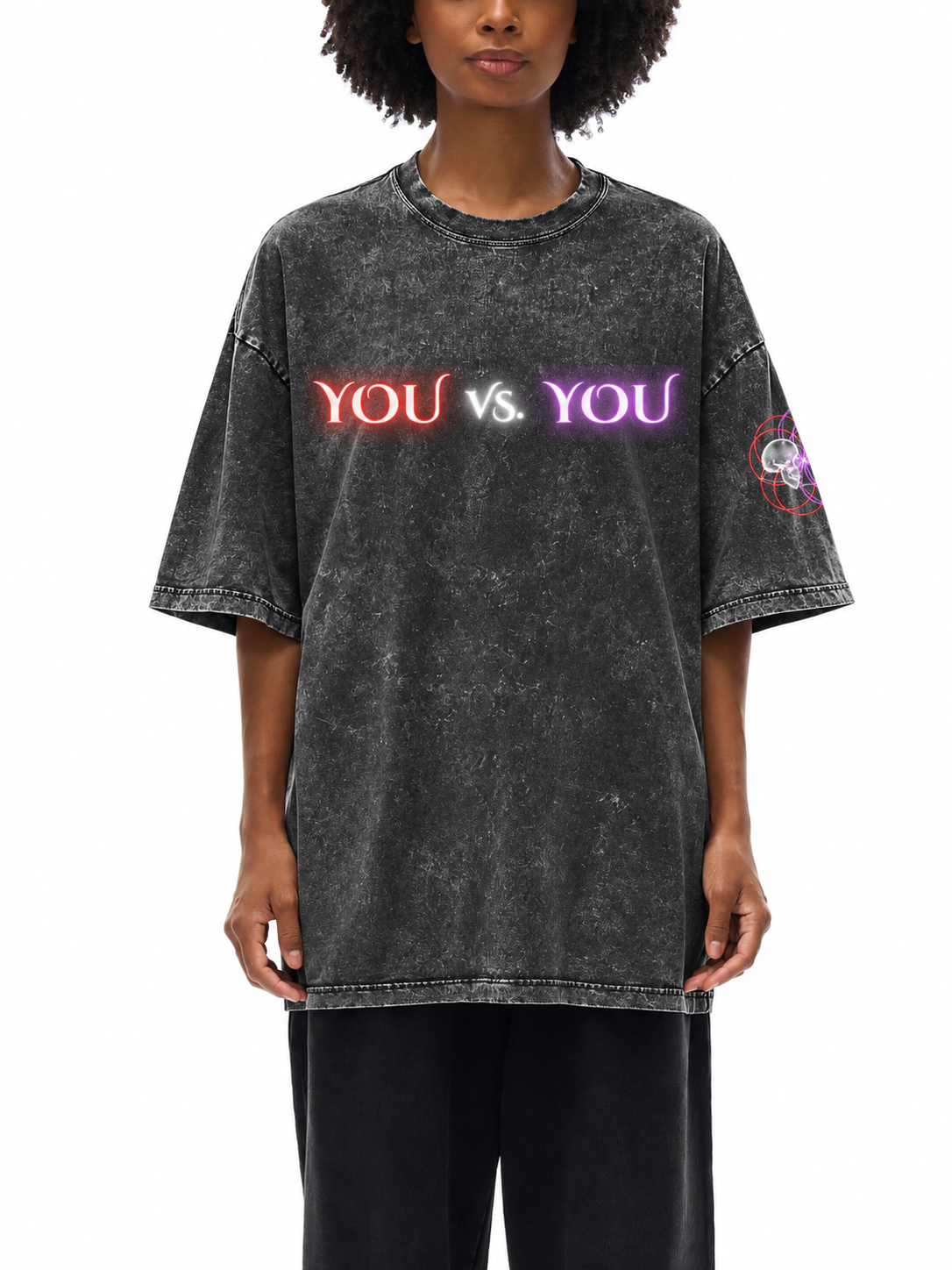 A model wearing an oversized, acid-washed black t-shirt with 'YOU vs. YOU' printed across the chest in red, white, and purple neon-style lettering, paired with black pants against a white background.